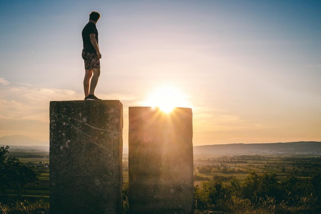 A man stands on stone blocks at sunset, gazing over a scenic Austrian landscape, evoking themes of solitude and exploration.